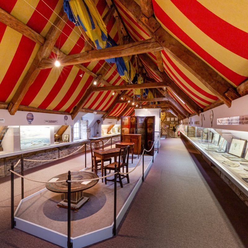 alt="Salle d’exposition du Musée des Ballons avec maquettes de montgolfières et objets historiques liés à l’aérostation"