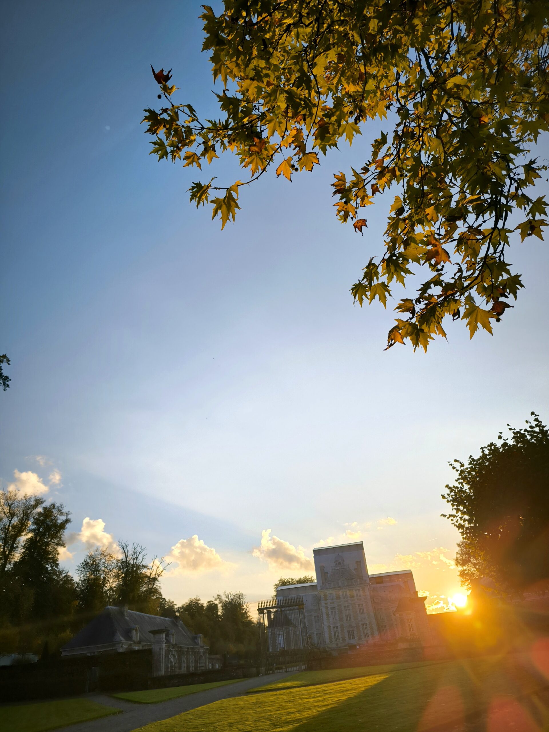 alt="Coucher de soleil derrière le Château de Balleroy, baignant le domaine dans une lumière dorée"