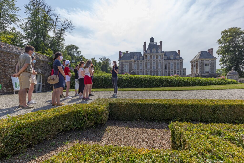 alt="Guide en train d'accueillir un groupe de visiteurs devant les jardins à la française"